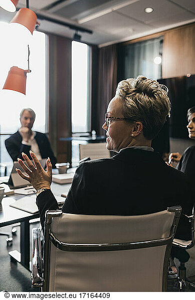 Rear view of mature female professional gesturing while explaining during meeting in board room