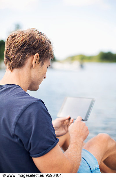 Rear view of mature man using digital tablet at lake