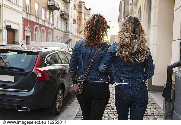 Rear view of mother and daughter walking at roadside in city