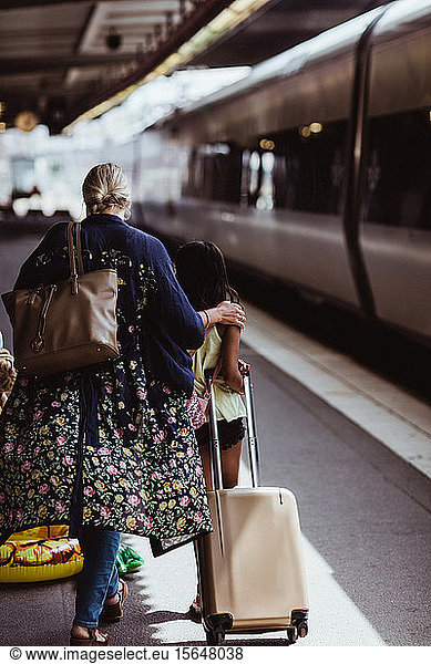 Rear view of mother and daughter walking with luggage on railroad station platform