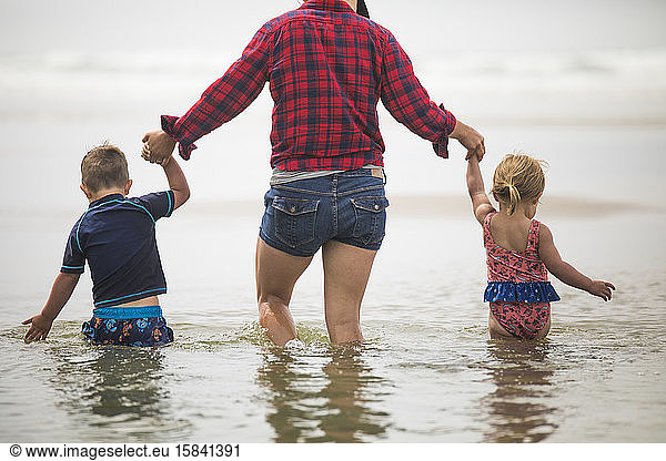 rear view of mother helping kids wade through water at the beach.