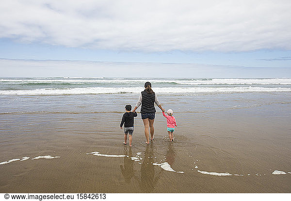 Rear view of mother walking toward ocean holding hands of her two kids