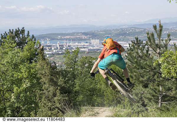 Rear view of mountain biker performing jump stunt on his bike