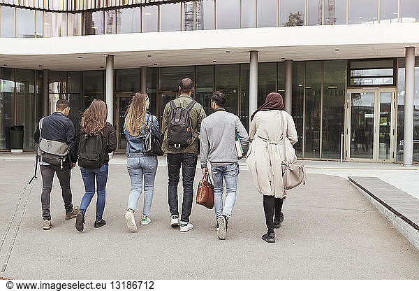 Rear view of multi-ethnic students walking against building in high school campus