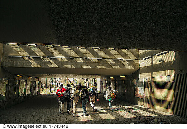 Rear view of multiracial friends walking together through underpass