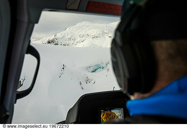 rear view of passenger looking out window of helicopter at glacier