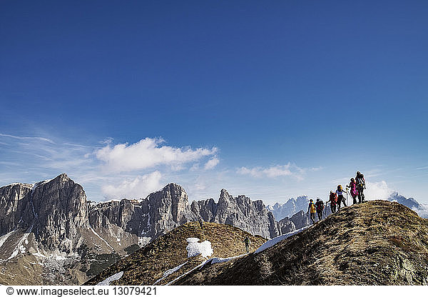 Rear view of people hiking on mountain against blue sky