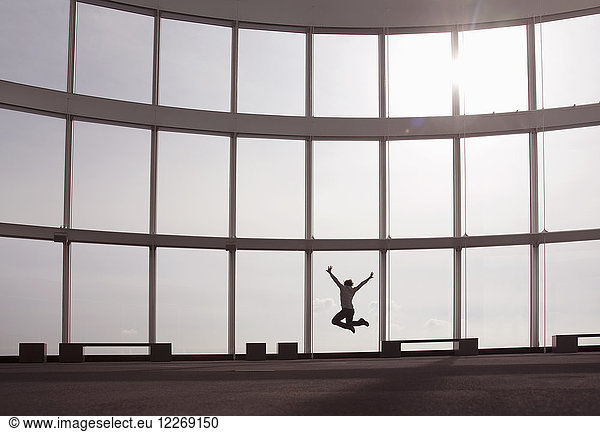 Rear view of person jumping in the air in front of tall glass wall.