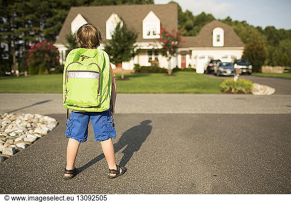 Rear view of schoolboy with backpack standing on street during sunny day