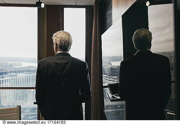 Rear view of senior businessman standing by reflection on television in board room