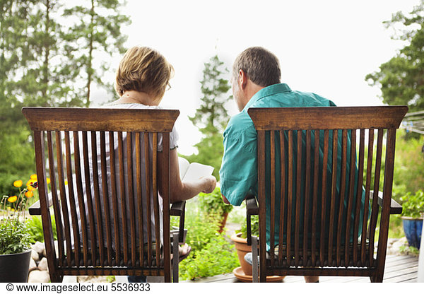Rear view of senior couple reading book together in back yard