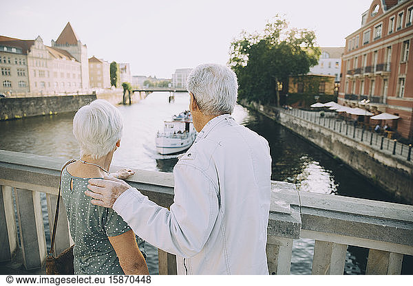 Rear view of senior couple standing on bridge against railing in city