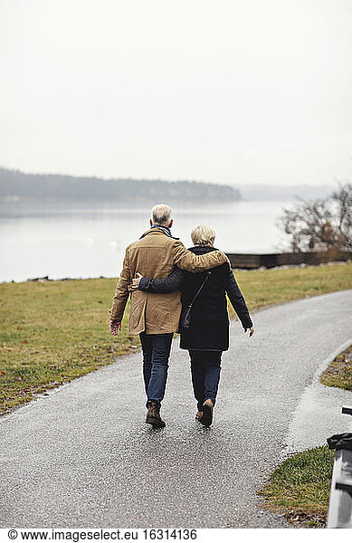 Rear view of senior couple with arm around walking on footpath during winter