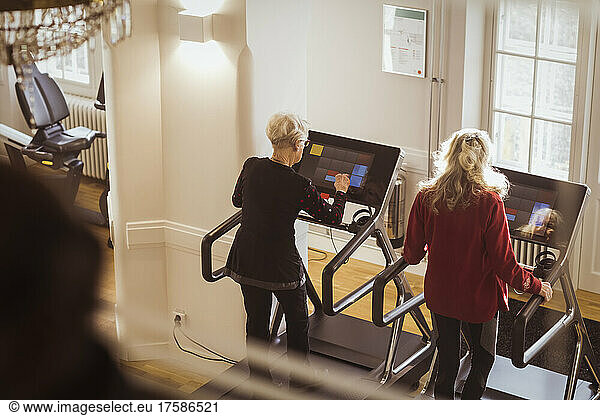 Rear view of senior female friends exercising on treadmill at retirement home