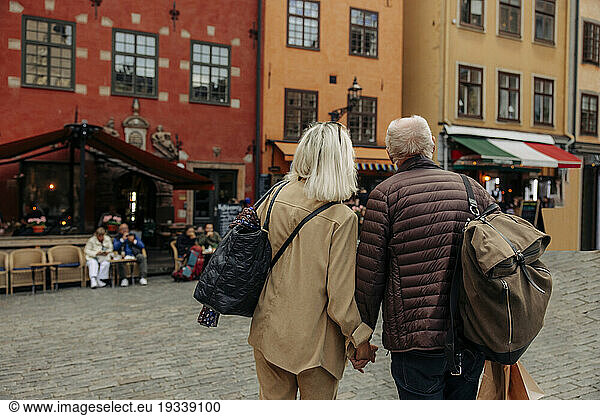 Rear view of senior tourist couple holding hands while walking together in city