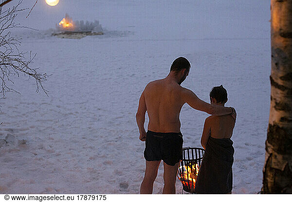 Rear view of shirtless father standing with son by bonfire at night