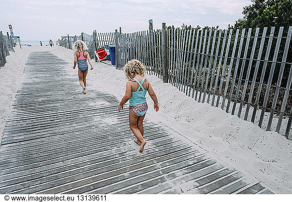 Rear view of sisters in swimwear walking on boardwalk