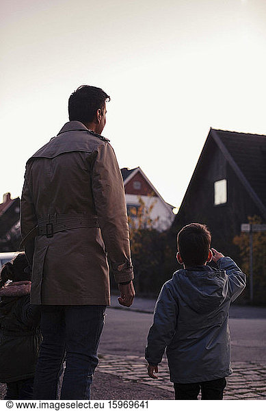 Rear view of son pointing while standing by father on footpath during sunset