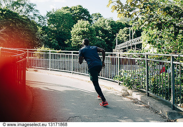 Rear view of sportsman jogging on footbridge in city