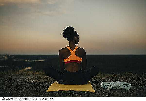 Rear view of sportswoman sitting on exercise mat during sunset