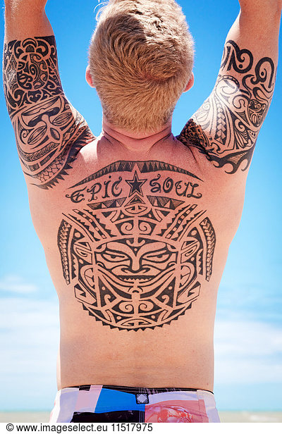 Rear view of tattooed man with arms raised
