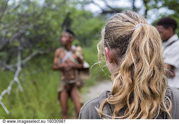 Rear view of teen girl walking with a group of bushmen from the San people.