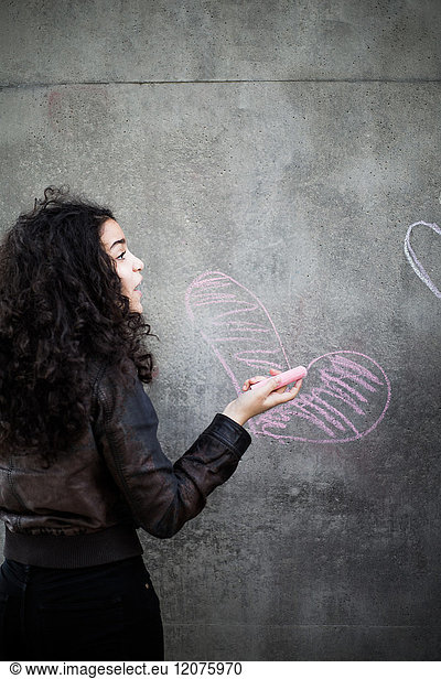 Rear view of teenage girl drawing heart shape on wall with pink chalk