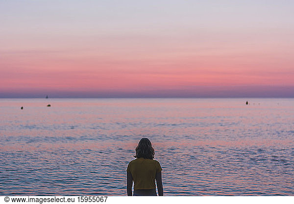 Rear view of teenage girl looking at horizon over sea during sunrise, Rear view of teenage girl looking at horizon over sea during sunrise