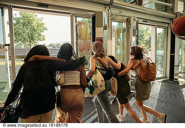 Rear view of teenage girls with arms around leaving shopping mall