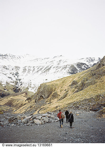 Rear view of three tourists walking toward snow capped mountains  Iceland