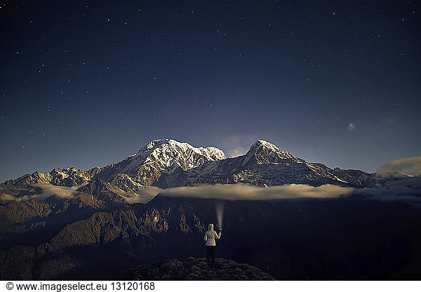 Rear view of tourist holding flashlight while standing on mountain against sky at night