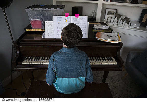 Rear View of Tween Boy Playing Piano at Home From Marked Pages in Book