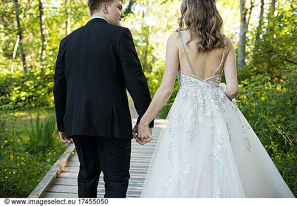 Rear view of well-dressed couple holding hands outdoors.