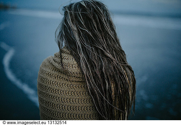 Rear view of wet woman with scarf standing at beach at dusk