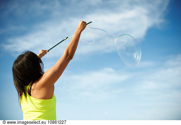 Rear view of woman  arms raised using bubbles wands to make bubbles