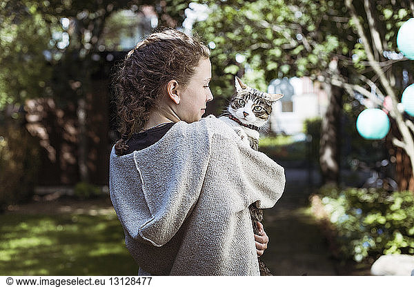 Rear view of woman carrying cat while standing in backyard