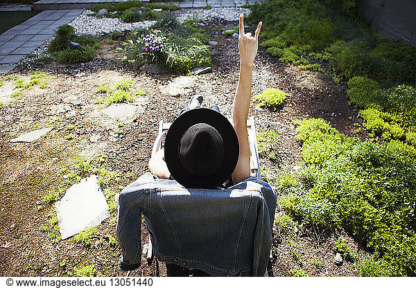 Rear view of woman gesturing horn sign while sitting on deck chair at terrace