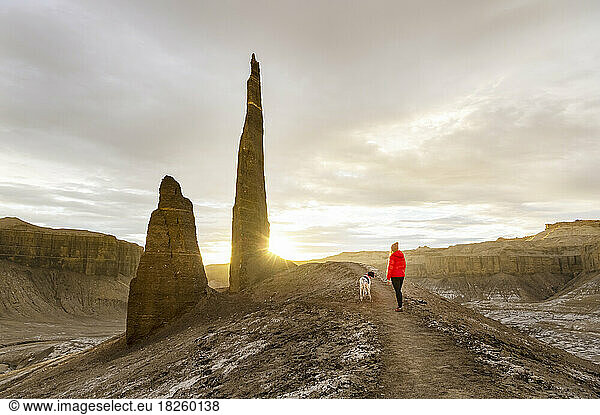 Rear view of woman hiking with dog at desert during sunset