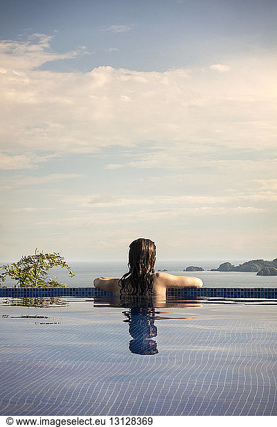 Rear view of woman in swimming pool enjoying view of Costa Rica against cloudy sky