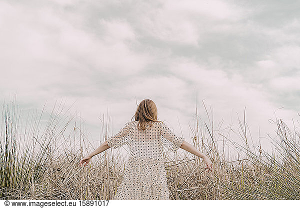Rear view of woman in vintage dress with outstretched arms at a remote field in the countryside, Rear view of woman in vintage dress with outstretched arms at a remote field in the countryside