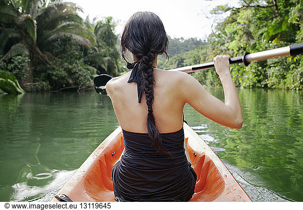 Rear view of woman kayaking on lake at forest