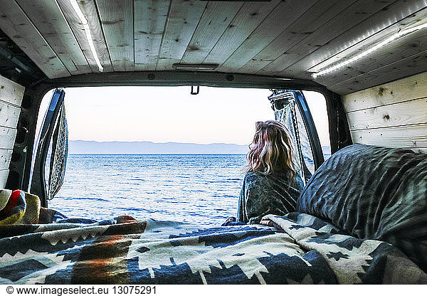 Rear view of woman looking at sea while leaning against travel trailer, Rear view of woman looking at sea while leaning against travel trailer