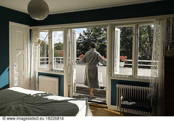 Rear view of woman opening doors of bedroom while walking in balcony