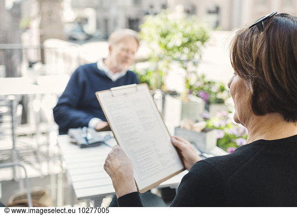 Rear view of woman reading menu while man sitting at sidewalk cafe