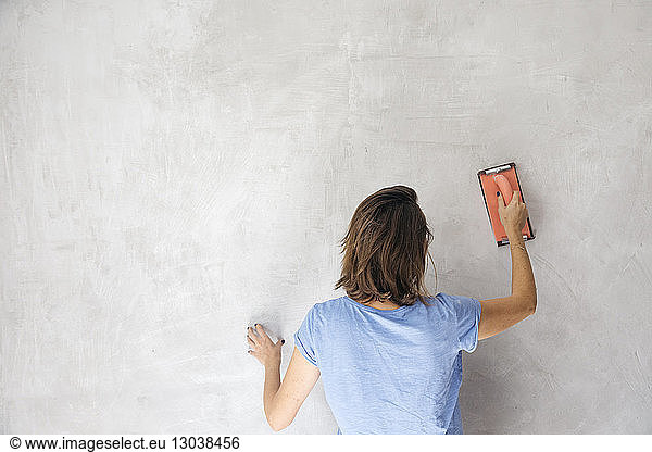 Rear view of woman sanding wall with hand sander