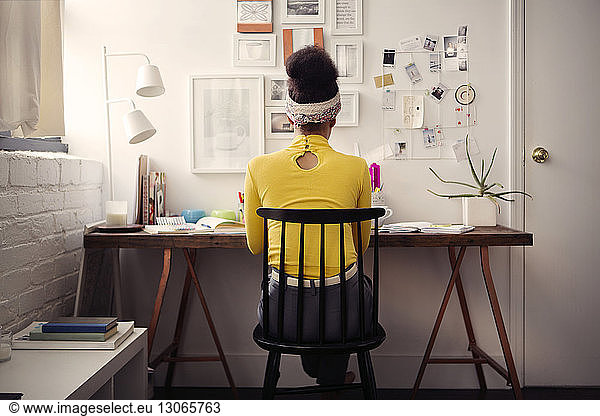 Rear view of woman sitting at table against papers on wall