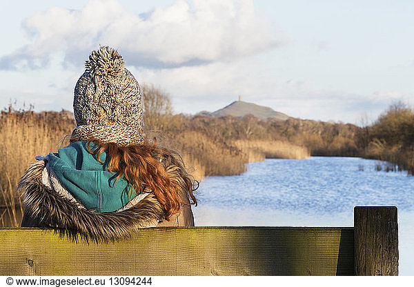 Rear view of woman sitting on bench at riverbank during winter, Rear view of woman sitting on bench at riverbank during winter