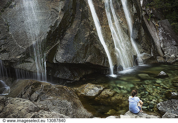 Rear view of woman sitting on rock against waterfalls