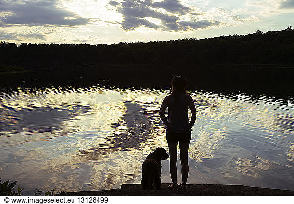 Rear view of woman standing by lake with dog