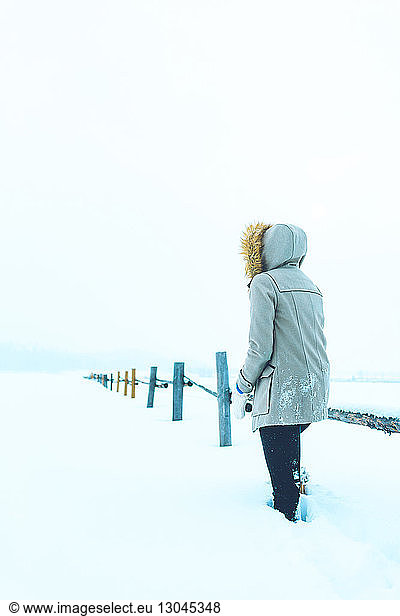 Rear view of woman standing by railing on snow covered field, Rear view of woman standing by railing on snow covered field